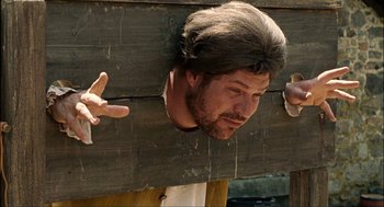 Movie still from “Choke” (2008), directed by Clark Gregg – A man with long hair is hanging from a wooden beam; Medium shot, Over the shoulder angle