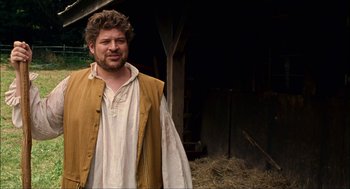 Movie still from “Choke” (2008), directed by Clark Gregg – A man standing next to a pile of hay; Medium shot, Over the shoulder angle