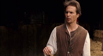 Movie still from “Choke” (2008), directed by Clark Gregg – A man holding a wooden stick while standing in front of a wall; Close Up shot, Over the shoulder angle