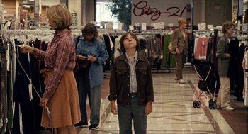 Movie still from “Choke” (2008), directed by Clark Gregg – A young boy standing in front of a group of people; Wide shot, Over the shoulder angle