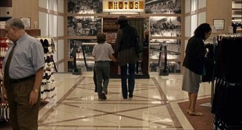 Movie still from “Choke” (2008), directed by Clark Gregg – A woman and a child are walking in a mall; Wide shot, Over the shoulder angle