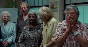 Movie still from “Choke” (2008), directed by Clark Gregg – A group of women standing next to each other in a room; Medium shot, Low angle