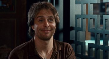 Movie still from “Choke” (2008), directed by Clark Gregg – A person wearing a brown shirt smiling; Close Up shot, Over the shoulder angle