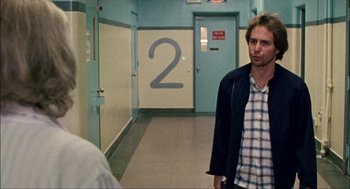 Movie still from “Choke” (2008), directed by Clark Gregg – A man standing in the hallway of a building; Medium shot, Over the shoulder angle