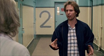 Movie still from “Choke” (2008), directed by Clark Gregg – A man standing in front of a number two sign; Medium shot, Over the shoulder angle