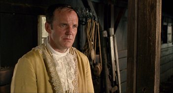 Movie still from “Choke” (2008), directed by Clark Gregg – A man in a yellow jacket standing next to a wall; Close Up shot, Over the shoulder angle