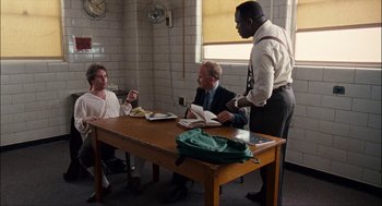 Movie still from “Choke” (2008), directed by Clark Gregg – Three men sitting at a table in front of a window; Wide shot, High angle