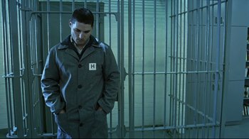 Movie still from “Chopper” (2000), directed by Andrew Dominik – A man standing in front of a metal cage; Medium shot, Low angle