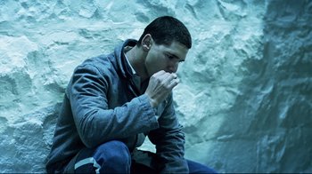 Movie still from “Chopper” (2000), directed by Andrew Dominik – A man sitting on the ground in front of a rock wall; Medium shot, High angle