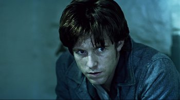 Movie still from “Chopper” (2000), directed by Andrew Dominik – A young man with dark brown hair and blue eyes stares straight ahead; Close Up shot, Low angle