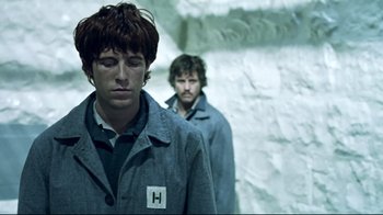 Movie still from “Chopper” (2000), directed by Andrew Dominik – Two men standing next to each other in front of a stone wall; Medium shot, Over the shoulder angle