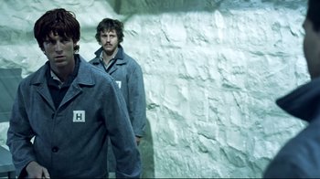 Movie still from “Chopper” (2000), directed by Andrew Dominik – Two men standing next to each other in front of a stone wall; Medium shot, Over the shoulder angle