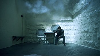 Movie still from “Chopper” (2000), directed by Andrew Dominik – A man sitting on a chair in a dimly - lit room; Wide shot, Low angle