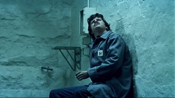 Movie still from “Chopper” (2000), directed by Andrew Dominik – A man sitting on a chair in a room; Medium shot, Low angle