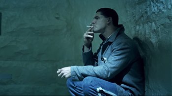 Movie still from “Chopper” (2000), directed by Andrew Dominik – A man smoking a cigarette while sitting on the ground; Medium shot, High angle