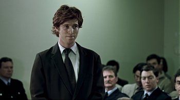 Movie still from “Chopper” (2000), directed by Andrew Dominik – A man in a suit and tie standing in front of other people; Close Up shot, Over the shoulder angle