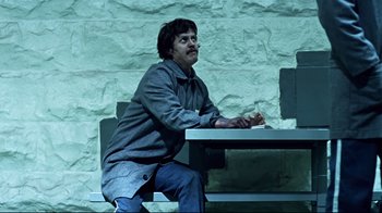Movie still from “Chopper” (2000), directed by Andrew Dominik – A man sitting at a table in front of a brick wall; Medium shot, Low angle