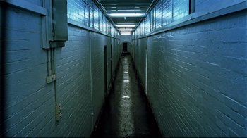 Movie still from “Chopper” (2000), directed by Andrew Dominik – A long hallway in a building with a brick wall; Wide shot, High angle