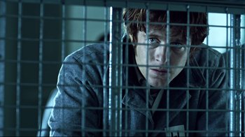 Movie still from “Chopper” (2000), directed by Andrew Dominik – A young man looking through a metal fence; Medium shot, Low angle