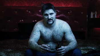 Movie still from “Chopper” (2000), directed by Andrew Dominik – A man sitting on the ground with a cigarette and beer; Medium shot, Low angle