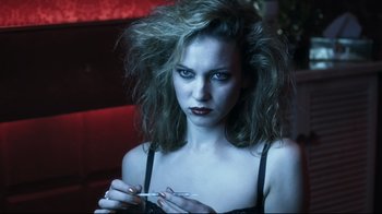 Movie still from “Chopper” (2000), directed by Andrew Dominik – A young woman is smoking a cigarette in a dark room; Close Up shot, Low angle