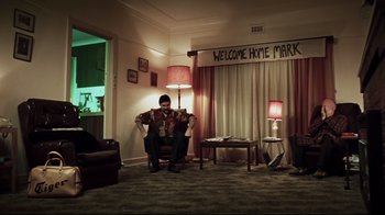 Movie still from “Chopper” (2000), directed by Andrew Dominik – A man sitting in a chair in a living room; Wide shot, Low angle