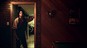 Movie still from “Chopper” (2000), directed by Andrew Dominik – A man standing in front of a wall clock; Medium shot, Low angle