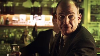 Movie still from “Chopper” (2000), directed by Andrew Dominik – A man in a suit and tie sitting in front of a bar; Close Up shot, Over the shoulder angle