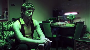 Movie still from “Chopper” (2000), directed by Andrew Dominik – A man sitting at a table with a cigarette in his mouth; Medium shot, Low angle