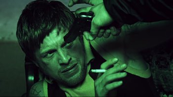 Movie still from “Chopper” (2000), directed by Andrew Dominik – A man with a cigarette in his mouth and another man taking a picture of him; Close Up shot, Low angle