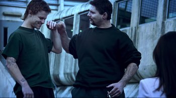 Movie still from “Chopper” (2000), directed by Andrew Dominik – A man and a young boy fist bumping each other; Medium shot, Over the shoulder angle