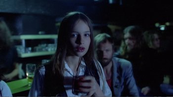 Movie still from “Christiane F.” (1981), directed by Uli Edel – A woman holding a drink in her hand while standing next to a man; Medium shot, Over the shoulder angle