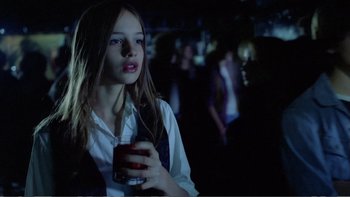 Movie still from “Christiane F.” (1981), directed by Uli Edel – A woman holding a drink in a dark room; Medium shot, Over the shoulder angle
