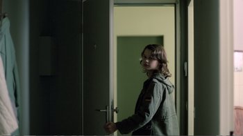 Movie still from “Christiane F.” (1981), directed by Uli Edel – A young girl standing in front of an open door; Medium shot, Over the shoulder angle