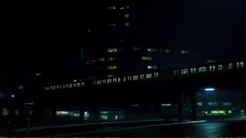 Movie still from “Christiane F.” (1981), directed by Uli Edel – A train traveling down tracks next to a tall building at night; Extreme Wide shot, Low angle