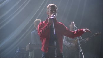 Movie still from “Christiane F.” (1981), directed by Uli Edel – A man in a red jacket is singing into a microphone; Medium shot, Low angle