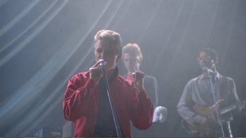 Movie still from “Christiane F.” (1981), directed by Uli Edel – A man holding a microphone in front of a crowd; Medium shot, Low angle