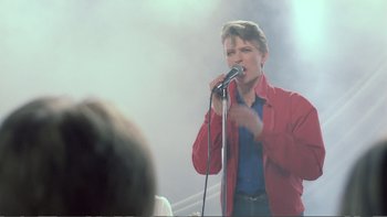 Movie still from “Christiane F.” (1981), directed by Uli Edel – A man in a red jacket is singing into a microphone; Medium shot, Over the shoulder angle