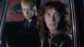Movie still from “Christiane F.” (1981), directed by Uli Edel – Two young men sitting next to each other in a dark room; Close Up shot, Low angle
