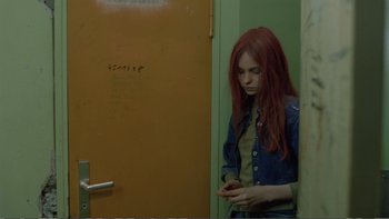 Movie still from “Christiane F.” (1981), directed by Uli Edel – A woman with red hair is leaning against a door; Medium shot, Over the shoulder angle