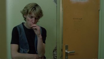 Movie still from “Christiane F.” (1981), directed by Uli Edel – A man leaning against a wall in front of a door; Medium shot, Low angle