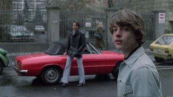 Movie still from “Christiane F.” (1981), directed by Uli Edel – Two young men standing in front of a red car; Medium shot, Over the shoulder angle