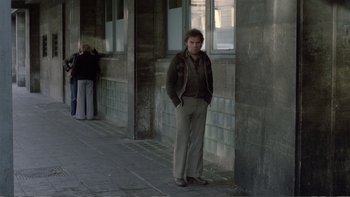 Movie still from “Christiane F.” (1981), directed by Uli Edel – A man standing in front of a building with his hands in his pockets; Wide shot, Over the shoulder angle