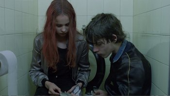 Movie still from “Christiane F.” (1981), directed by Uli Edel – A girl and a boy are looking at a cell phone; Medium shot, Over the shoulder angle
