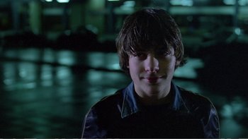 Movie still from “Christiane F.” (1981), directed by Uli Edel – A young man is smiling for the camera in the dark; Close Up shot, Over the shoulder angle