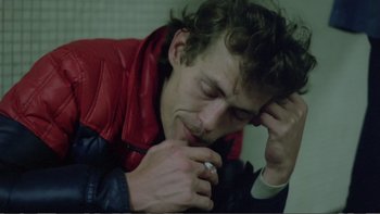 Movie still from “Christiane F.” (1981), directed by Uli Edel – A man in a red jacket holding his hand to his face; Close Up shot, High angle