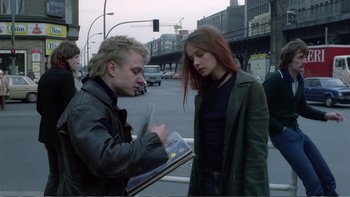Movie still from “Christiane F.” (1981), directed by Uli Edel – A man and a woman standing next to each other on a street; Medium shot, Over the shoulder angle