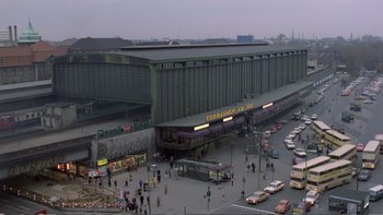Movie still from “Christiane F.” (1981), directed by Uli Edel – An aerial view of a train station with a lot of cars parked on the side; Extreme Wide shot, High angle
