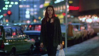 Movie still from “Christiane F.” (1981), directed by Uli Edel – A woman walking down a street holding a bag of food; Wide shot, Low angle