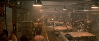 Movie still from “Christine” (1983), directed by John Carpenter – A group of people standing around a car shop; Extreme Wide shot, High angle